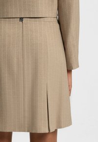 Beige, pinstriped fabric with a fitted waist, featuring a zipper closure and a side slit for ease of movement.