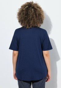 Námořnická modrá krátkosrstá blůza vyrobená z lehké látky, s kulatým lemem a jemnou texturou. Zadní pohled ukazuje jednoduchý design.