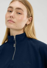 Felpa blu navy con colletto alto, chiusura a mezza zip e logo ricamato. Texture morbida con vestibilità rilassata, caratterizzata da maniche raglan.