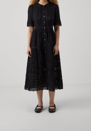 Robe midi noire avec fermeture à boutons sur le devant, détails en dentelle sur les manches et la jupe, portée avec des chaussures Mary Jane noires cloutées.
