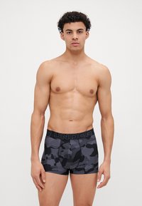 Boxer shorts de camuflaje en negro y gris con una amplia cintura elástica que muestra el texto "UNDER". Material elástico, diseño ajustado.