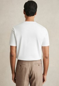Tricou alb cu mânecă scurtă și guler rotund, asortat cu pantaloni bej deschis, ajustați, având două buzunare la spate cu nasturi.