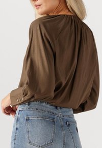 Bruine, lichtgewicht, blouse met lange mouwen en een geplooide halslijn, met knoopmanchetten, gecombineerd met lichtblauwe, hoge Taille spijkerbroeken.