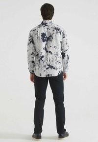 Chemise à manches longues avec un motif floral blanc et marine, en tissu léger ; associée à un pantalon noir et des chaussures décontractées.