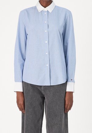 Osoba ubrana w niebieską i białą koszulę w paski z białym kołnierzykiem i mankietami, w połączeniu z ciemnoszarymi dżinsami.