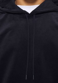 Schwarze Cord-Hoodie mit einer Kordelzugkapuze, gerippter Textur und bequemer Passform, mit silbernen Ösen an den Kordeln.