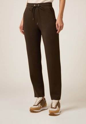 Pantalon de jogging marron avec une taille à cordon, en tissu doux, jambes fuselées et poches latérales. Associé à des baskets crème et marron.