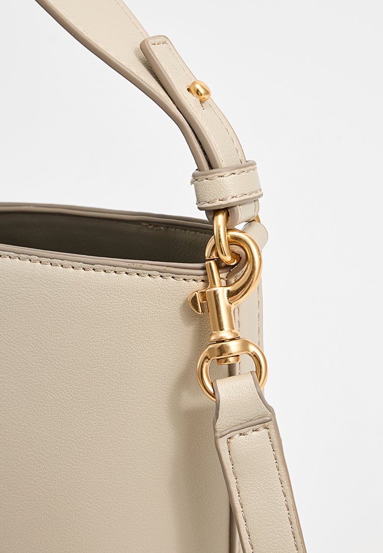Beige Lederhandtasche mit glatter Textur, goldenen Beschlägen und einem stabilen, verstellbaren Tragegurt mit Clipbefestigung.