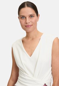 Biała bezrękawnikowa bluzka z głębokim dekoltem w kształcie V, z drapowanym materiałem i węzłem w talii, gładka tekstura i minimalistyczny design.