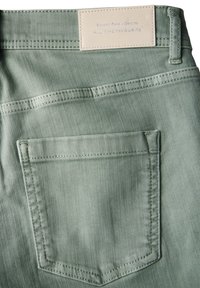 Pantalones de mezclilla verdes con un bolsillo trasero, detalles de costura sutiles y una etiqueta de cuero con el nombre de la marca en la cintura.