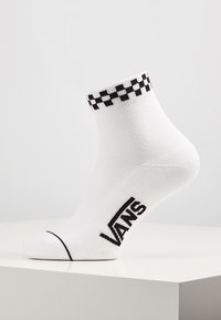 Weißer Baumwollsocke mit einem schwarzen Schachbrettmuster am Bündchen und einem kontrastierenden schwarzen "VANS"-Logo an der Seite. Höhe bis zur Mitte der Wade.