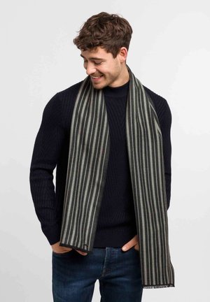 Striped scarf in gray and black, made of textured fabric, displaying vertical stripes with frayed ends. Worn draped over a dark sweater.