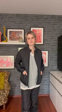 Crna bomber jakna glatke teksture, nosi se preko svijetlog uzorka majice i tamnih hlača. U pozadini su okviri sa umjetničkim djelima i udobna stolica.