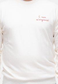 Felpa color crema realizzata in materiale morbido, con testo ricamato rosso sulla parte sinistra del petto. Collo a giro classico e polsini aderenti.