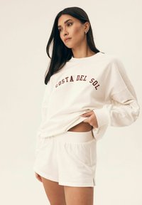 Kremowa bluza z haftem "COSTA DEL SOL" w burgundowym kolorze, w komplecie z pasującymi kremowymi szortami. Miękki, casualowy materiał o luźnym kroju.