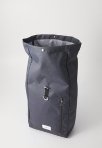 Zaino roll-top di colore grigio scuro, realizzato in tessuto resistente, dotato di una tasca frontale con zip, una chiusura a scatto e un accent metallico a forma di D.