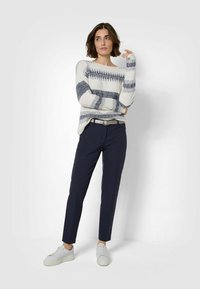 Maglione lavorato a maglia con righe navy e bianche, abbinato a pantaloni navy e sneaker bianche. Presenta una vestibilità rilassata e con polsini arrotolati.