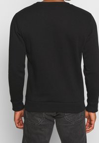 Felpa nera con maniche lunghe, scollo rotondo, polsini e orlo a coste. Realizzata in tessuto morbido, presenta una texture liscia e un design minimale.