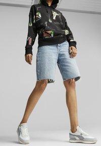 Sudadera negra con estampados gráficos coloridos, pantalones cortos de mezclilla claros con bordes deshilachados y zapatillas blancas con acentos grises.
