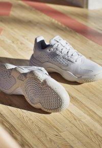 Baskets de sport blanches avec un dessus en maille texturée, une languette rembourrée et une semelle en caoutchouc présentant un motif de grip circulaire.