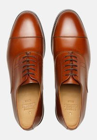Chaussures habillées en cuir marron avec une finition lisse, bouts ronds et six œillets. Présente des coutures discrètes et une semelle intérieure texturée.