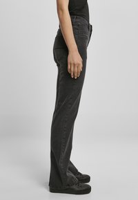 Jeans de mezclilla negros con corte recto, cintura media y un ligero desgastado. Presenta bolsillos laterales y detalles de costura. Combinados con zapatillas negras.