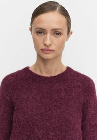 Burgundy stickad tröja med en mjuk, fluffig textur, med en klassisk rund halsringning och långa ärmar.