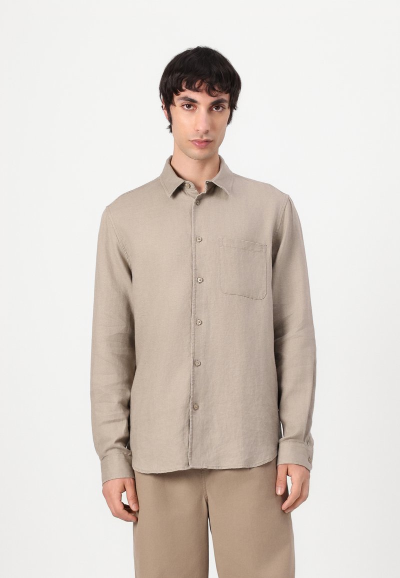 Camicia in lino beige a maniche lunghe con chiusura a bottoni, taschino sul petto e orlo arrotondato. Texture morbida con dettagli di cucitura visibili.