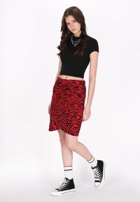 Fustă creion cu imprimeu zebră roșu și negru, cu talie ajustată și țesătură texturată, asortată cu un top scurt negru și adidași negri cu talpă înaltă.