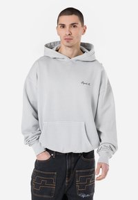 Sweatshirt cinza claro com um bolso canguru na frente, punhos canelados e logotipo bordado no peito. Tecido macio, corte descontraído.