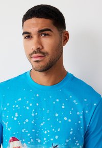 Modré bavlněné tričko s motivem zimní scény se sněhovými vločkami a obrazem Santy a soba. Kulatý výstřih, krátké rukávy.