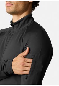 Maglia sportiva nera a maniche lunghe con colletto alto, texture liscia e una tasca con zip sulla manica con la scritta "SWEDEMOUNT."