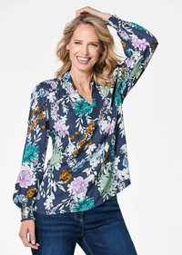 Blusa con fantasia floreale su sfondo blu navy, decorata con fiori colorati in verde, viola e giallo. Collo a V e maniche lunghe con polsini arricciati.