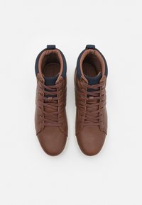 Zapatillas altas de cuero marrón con cuello de textil azul marino, cordones planos, detalles de costura y suelas de goma blanca.