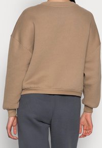 sweatshirt beige con una vestibilità rilassata, spalle scese, polsini e vita a costine, realizzato in un morbido tessuto misto cotone, mostrato da dietro.