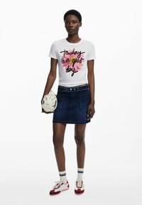 T-shirt blanc avec un graphique floral coloré et du texte, associé à une jupe en denim foncé avec des poches devant et des boutons décoratifs.