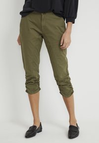 Olivgröna cropped byxor med rynkning vid fållarna, tillverkade av ett mjukt bomullsmaterial och en klassisk rak passform, i kombination med svarta loafers.