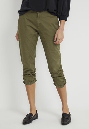 Un pantalon vert olive court avec des fronces aux ourlets, fabriqué à partir d'un matériau en coton doux, et un design droit classique associé à des mocassins noirs.