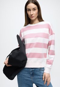 Ροζ και λευκή ριγέ μπλούζα με μακριά μανίκια και στρογγυλή λαιμόκοψη, σε συνδυασμό με μαύρη τσάντα tote και casual τζιν παντελόνι με ξεφτισμένες λεπτομέρειες.