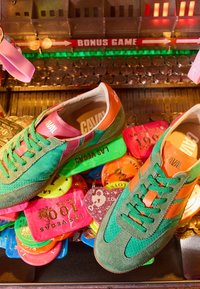 Des baskets vertes et orange reposent sur des jetons de casino colorés de Las Vegas et des pièces d'or sous les lumières d'un jeu d'arcade.