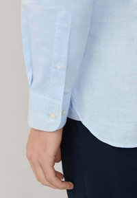 Lichtblauwe lange mouw shirt met subtiele textuur, knoopmanchetten met ronde, witte knopen en een gebogen zoom.