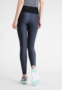 Leggings marinos con una cinturilla alta negra, que presentan una textura suave y detalles en las costuras, combinados con zapatos deportivos grises y suelas blancas.