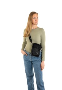 Borsa a tracolla in nylon nero con tracolla regolabile, tasca frontale e dettagli in metallo, indossata da un modello con un top attillato a maniche lunghe e jeans.