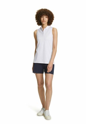 Haut polo sans manches blanc avec un col, associé à un short bleu marine et des baskets blanches. Texture lisse, design minimaliste, sans motifs.