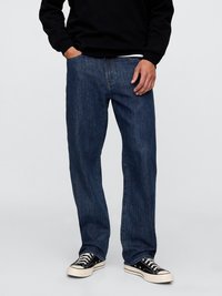 Blaue Jeans aus Denim mit geradem Bein, fünf Taschen, sichtbaren Nähten und einer leichten Verwaschung. Kombiniert mit schwarzen Sneakers.