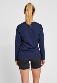 Mörkblå långärmad topp med rund hals och lätt stretch, i kombination med svarta shorts. Slät tyg och minimalistisk design utan mönster.