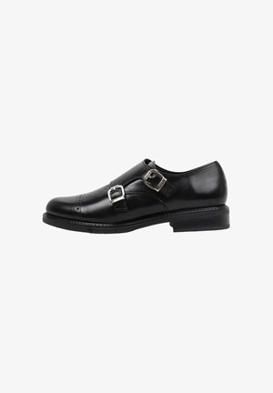 Chaussure de ville en cuir noir à fermoirs monks, avec deux boucles en argent, bout arrondi, perforations subtiles et un petit talon empilé. Texture lisse.