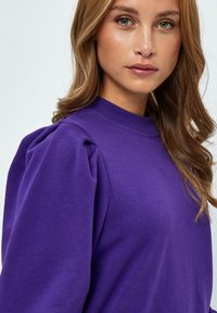 Lila sweatshirt med puffärmar, rund halsringning och en mjuk tygkänsla. Designen har en avslappnad passform och slät yta.