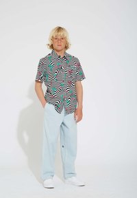 Chemise à manches courtes avec un motif de rayures ondulées noir et blanc, ornée d'accents floraux roses et verts, associée à un pantalon bleu clair.