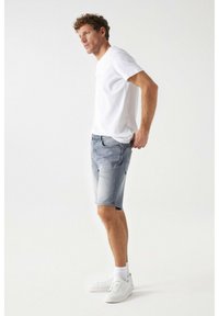 Shorts de denim gris con un acabado desgastado y cinco bolsillos, combinados con una camiseta blanca lisa y zapatillas blancas con suelas texturizadas.